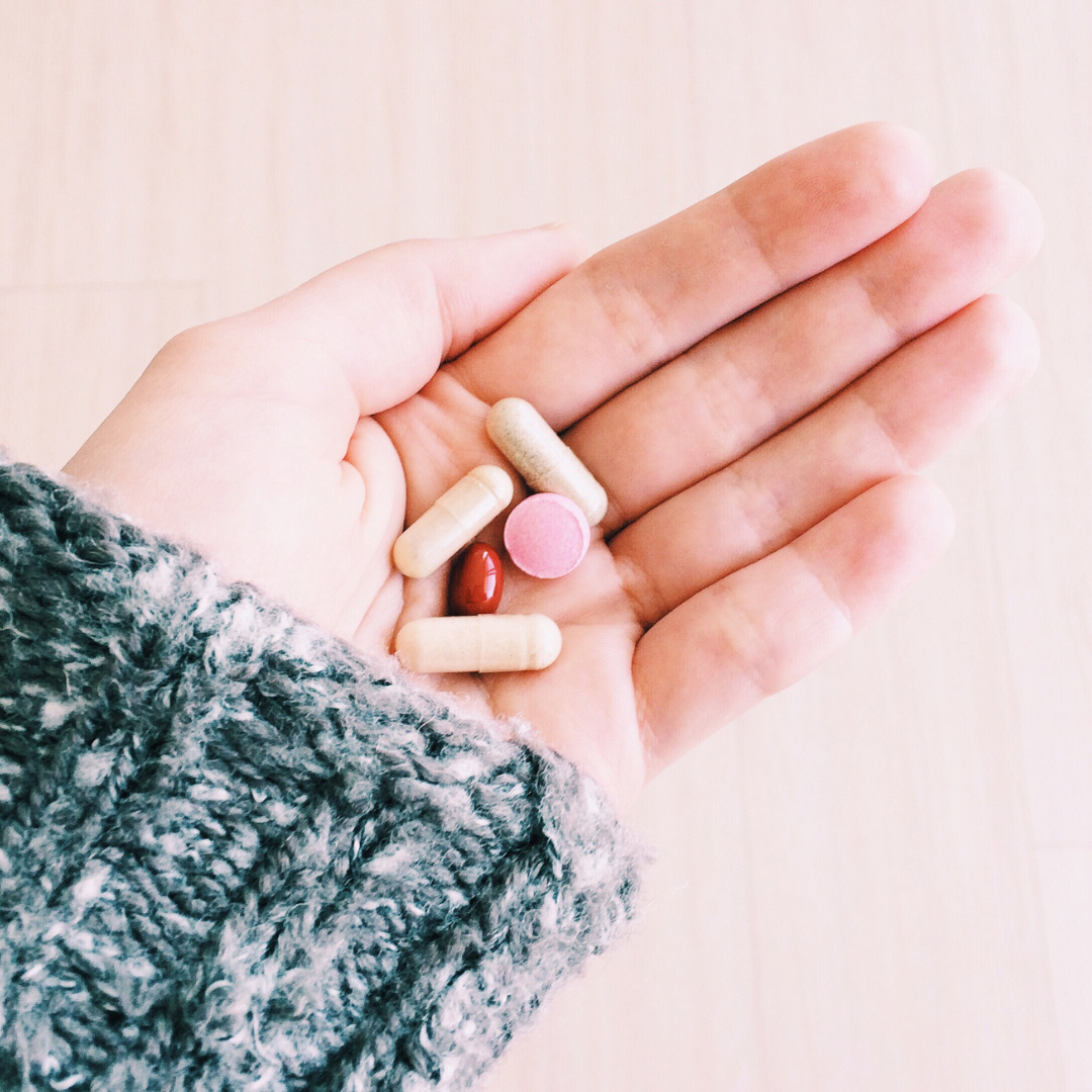 Open hand holding assorted pills and capsules of different sizes and colors.