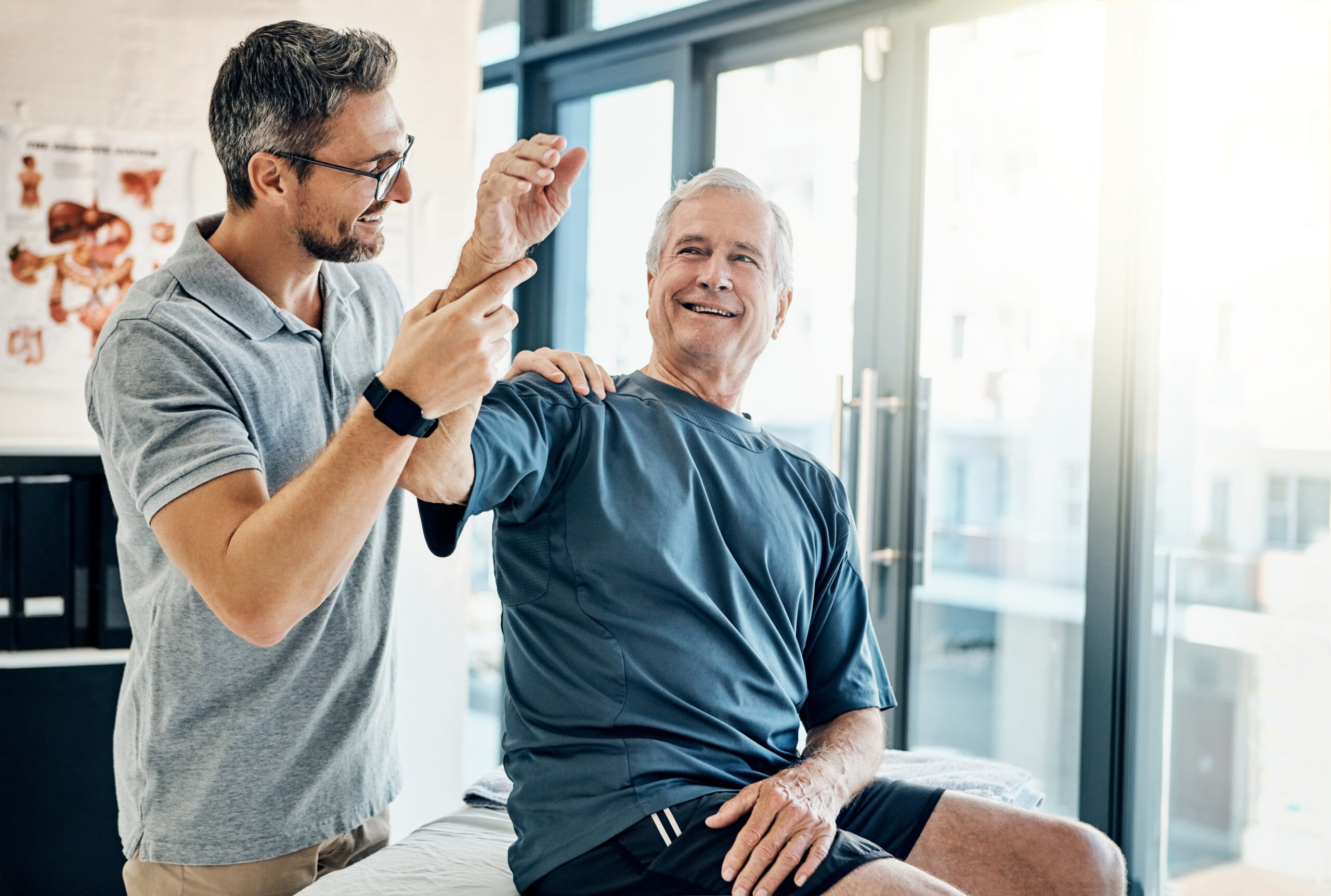 Male clinician giving a high-five to an older man in a medical clinic near large windows